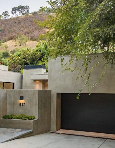 Modern house facade with concrete walls, black gate, and landscaped entryway.