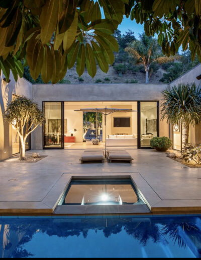 Modern house with pool at twilight, spacious patio, and open living area visible through glass doors.