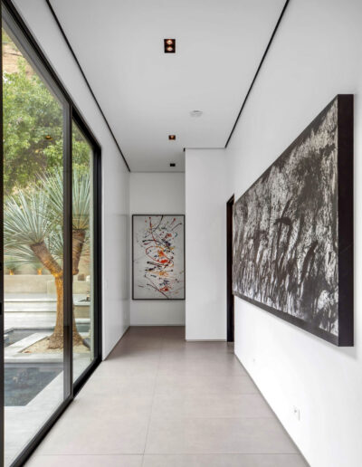 Minimalist hallway with large artwork, floor-to-ceiling windows, and a view of an outdoor palm tree.