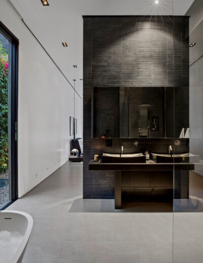 Modern bathroom interior with a freestanding bathtub, dual vanity, and a floor-to-ceiling window with a garden view.