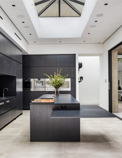 Modern kitchen with black cabinetry and stainless steel appliances, featuring a central island and skylights.