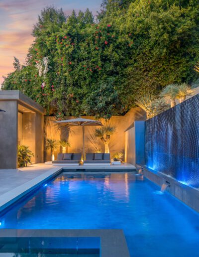 Luxurious backyard pool with a cascading water feature and ambient lighting at dusk.