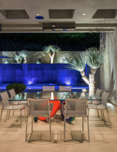 Modern outdoor patio with dining area and illuminated water feature at night.