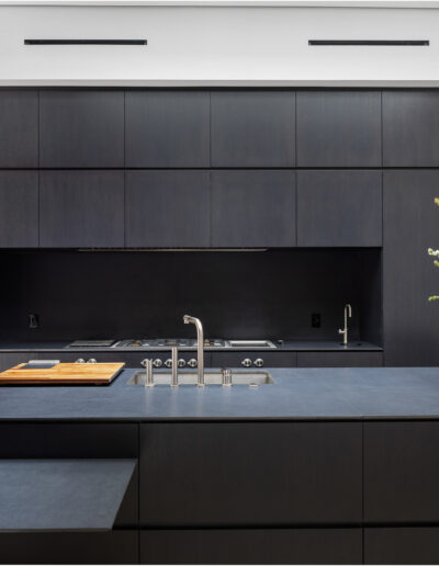 Modern kitchen with dark cabinetry and countertops, featuring a gas cooktop and a vase of white flowers.