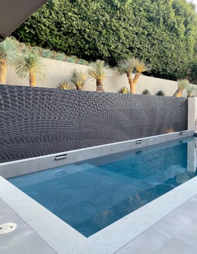 A modern pool with textured wall and palm trees in the background.