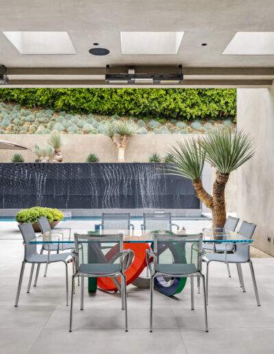 Modern outdoor dining area with colorful chairs, a wall-mounted waterfall, and a vertical garden.