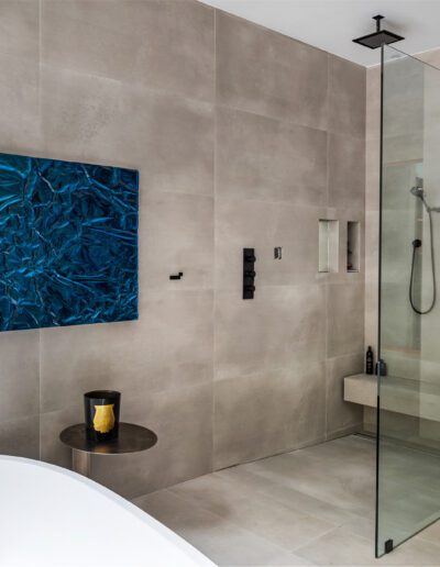 Modern bathroom with beige tiles, glass shower enclosure, and blue artwork.